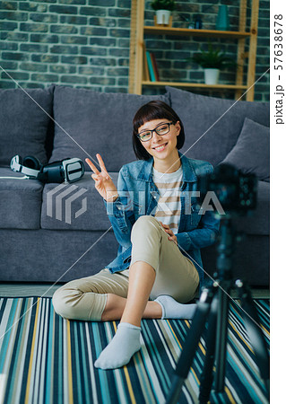 Cheerful woman in glasses is smiling and showing v-sign recording video at home 57638678