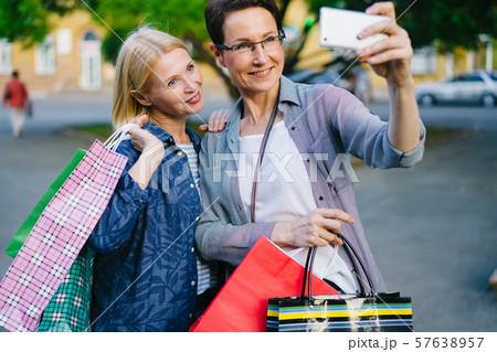 Attractive ladies using smartphone outdoors taking selfie with shopping bags 57638957
