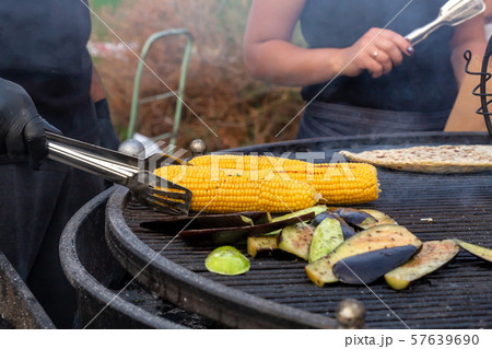 A cook fries corn and vegetables on a charcoal A cook fries corn and vegetables on a charcoal 57639690