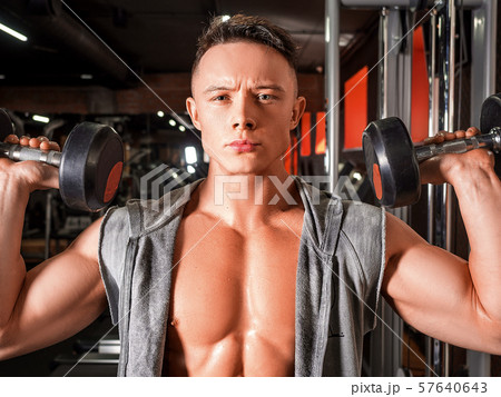 Shirtless man doing exercise for shoulders with dumbbells in gym. 57640643