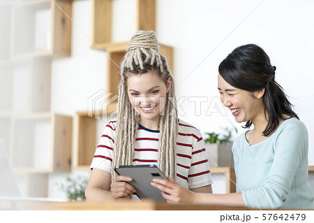 タブレットで楽しい動画ムービーを見て笑顔になる金髪のロシア人女性と日本人の写真素材