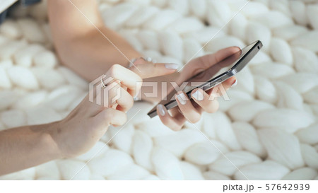A young girl lies on a white plaid in the park and dials a message on the phone. Hands close-up. A young girl lies on a white plaid in the park and dials a message on the phone. Hands close-up. 57642939