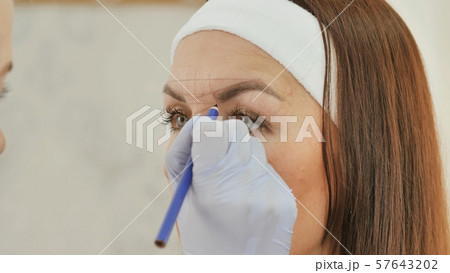 The girl beautician marks with the help of a pencil the future tattoo of eyebrows. 57643202