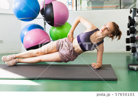 Sporty girl does a side plank exercise in a gym Sporty girl does a side plank exercise in a gym 57650103