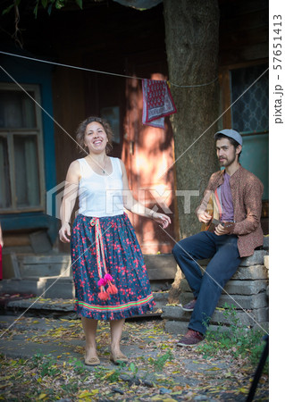 A smiling woman dancing near the country house and a man playing balalaika A smiling woman dancing near the country house and a man playing balalaika 57651413