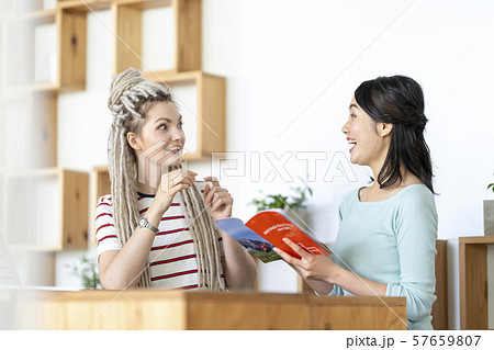 宮城県の観光案内パンフレットを見ながらサプライズな出来事を話す金髪の外国人女性と驚く日本人 57659807