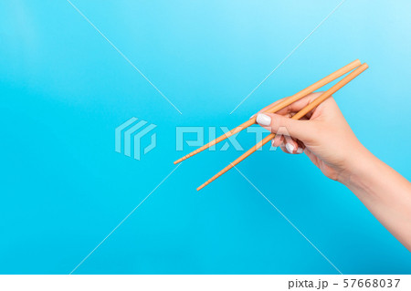 Female hand with chopsticks on blue background. 57668037