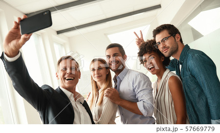 Happy moments. Group of smiling colleagues taking selfie and gesturing while standing in the modern Happy moments. Group of smiling colleagues taking selfie and gesturing while standing in the modern 57669779