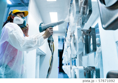 Powder coating of metal parts. A woman in a protective suit sprays white powder paint from a gun on Powder coating of metal parts. A woman in a protective suit sprays white powder paint from a gun on 57671092