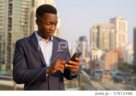 Young handsome African businessman using phone against view of the city 57672486