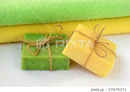 Green and yellow handmade soap bars near the same colors terry towels over a white one. 57676251