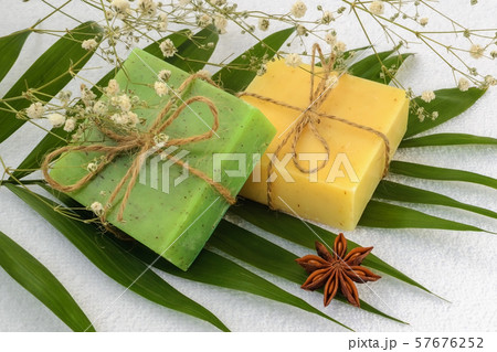 Green and yellow handmade soap bars on a green leaves over a white terry cotton towel. 57676252
