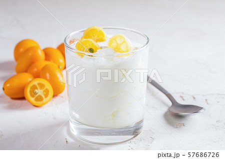 Close-up homemade yogurt with slices of exotic citrus fruit kumquat in transparent glass with whole fruits and metallic spoon on white background. 57686726