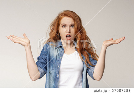 Confused Redhead Girl Shrugging Shoulders On Light Studio Background. 57687283