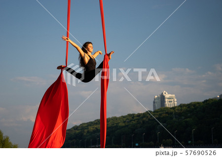 Beautiful and flexible female circus artist dancing with aerial silk with sky and river coastline on Beautiful and flexible female circus artist dancing with aerial silk with sky and river coastline on 57690526