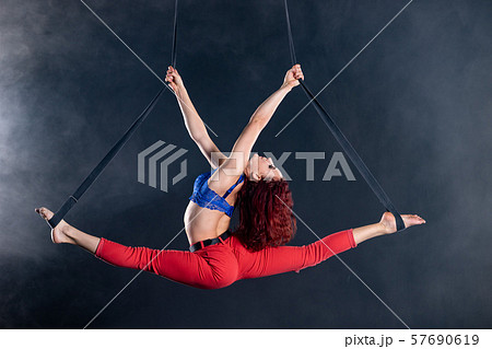 Female athletic, sexy and flexible aerial circus artist with redhead on aerial straps on black 57690619