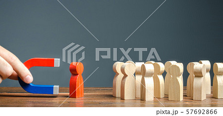 A hand with a red blue magnet pulls out a red human figure from the crowd. Search for talented workers with great career potential. Identify disloyal, repression, dissent. toxic, non-competent worker. 57692866