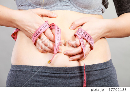 Woman touching stomach holding measuring tape Woman touching stomach holding measuring tape 57702183