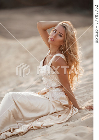 Portrait of beautiful bride is wearing fashion flying dress sitting on sand in the great desert in 57705762