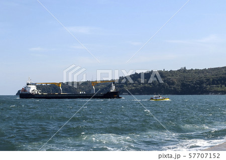 Small yellow pilot ship leads a large black cargo container ship to the seaport. Small yellow pilot ship leads a large black cargo container ship to the seaport. 57707152