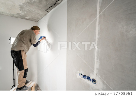 Young repairman aligns with plastic spatula. Worker glueing wallpapers on concrete wall. Repair the 57708961