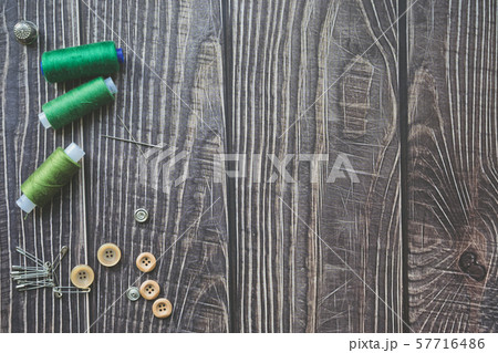Sewing accessories on dark wooden background. Green sewing threads, needle, buttons and pins. top 57716486