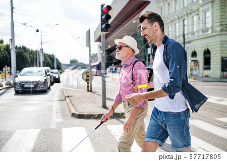 Young man and blind senior with white cane walking in city, crossing street. Young man and blind senior with white cane walking in city, crossing street. 57717805