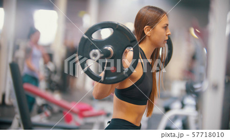 An athlete woman training in the gym - gets under the dumbbell and put it on her shoulders An athlete woman training in the gym - gets under the dumbbell and put it on her shoulders 57718010