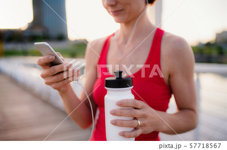 Midsection of young woman runner with earphones in city, using smartphone. Midsection of young woman runner with earphones in city, using smartphone. 57718567