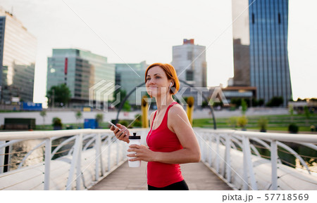 Young woman runner with earphones in city, using smartphone. 57718569