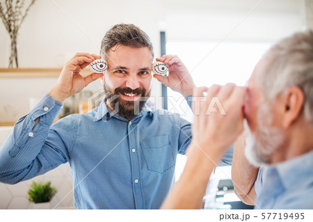 A portrait of adult hipster son and senior father indoors at home, having fun. A portrait of adult hipster son and senior father indoors at home, having fun. 57719495
