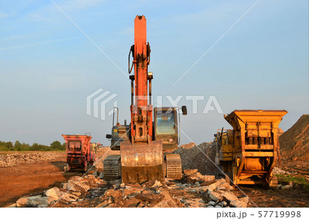 Heavy tracked excavator load stone, old asphalt or concrete waste into a mobile jaw crusher machine. 57719998