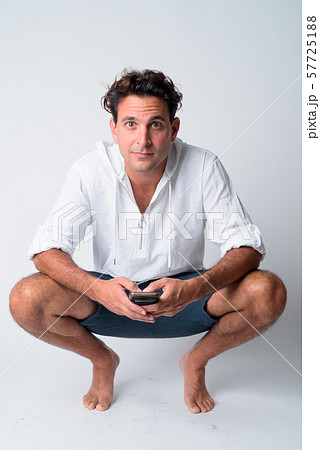 Full body shot of handsome Hispanic man crouching while holding phone Full body shot of handsome Hispanic man crouching while holding phone 57725188