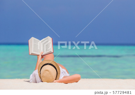 Portrait of a young woman relaxing on the beach, reading a book 57729481