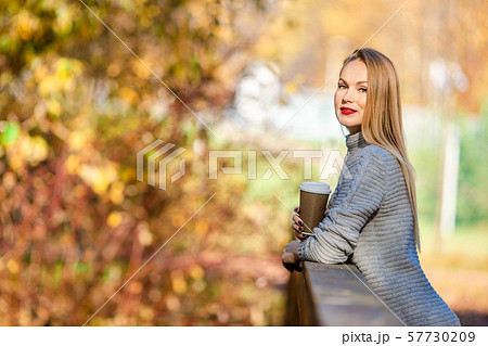 Fall concept - beautiful woman drinking coffee in autumn park under fall foliage 57730209