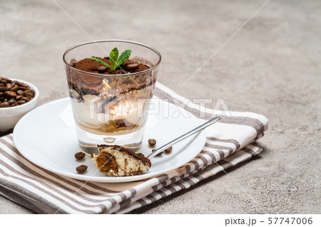 Portion of Classic tiramisu dessert in a glass cup on concrete background Portion of Classic tiramisu dessert in a glass cup on concrete background 57747006