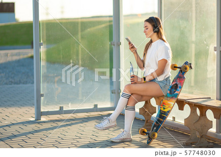 Stylish young girl sitting on bus stop with her 57748030