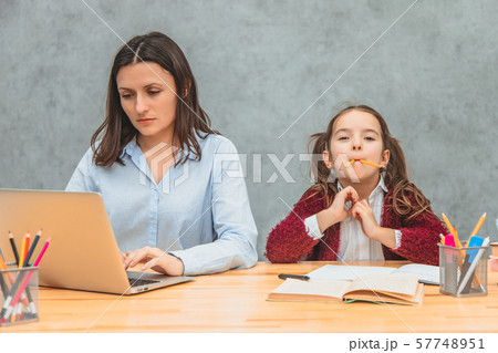 Daughter and mother on a gray background. During this, the girl puts the yellow pencils in her mouth Daughter and mother on a gray background. During this, the girl puts the yellow pencils in her mouth 57748951