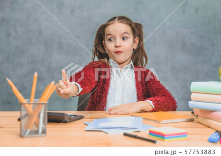 Schoolgirl girl sits at a gray background. During this, the index finger shows a yellow pencil 57753883