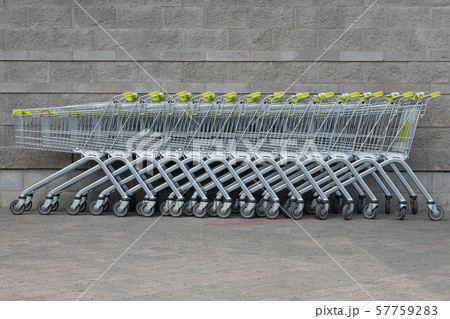 Many grocery carts with yellow handles standing in a row in the centre of photo by gray brick Many grocery carts with yellow handles standing in a row in the centre of photo by gray brick 57759283