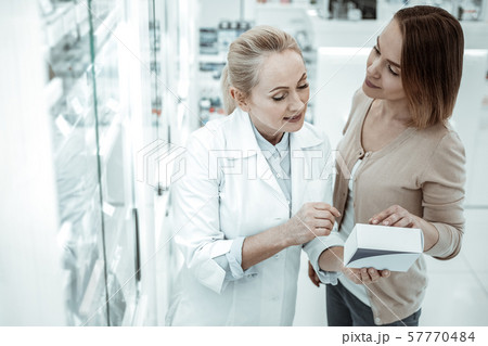 A pleasing druggist advising the female customer on vitamins ingredients A pleasing druggist advising the female customer on vitamins ingredients 57770484