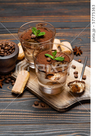Portion of Classic tiramisu dessert in a glass and savoiardi cookies on wooden background 57775363