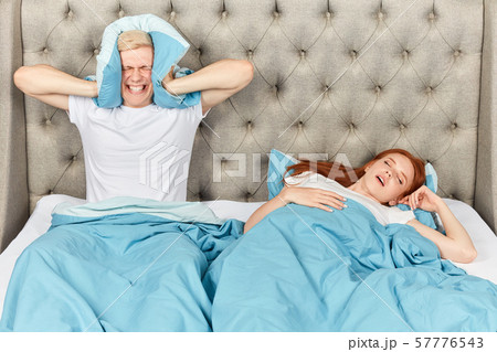 Angry young man closing his ears with pillow Angry young man closing his ears with pillow 57776543