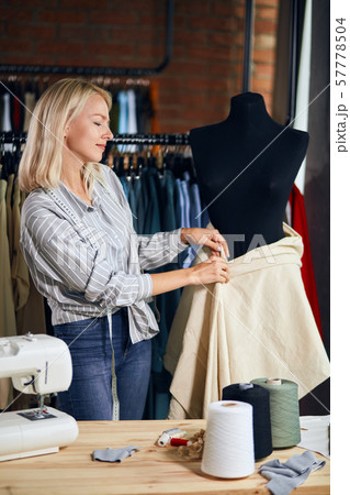 blonde femalen designer measuring fabric on black dummy at work 57778504