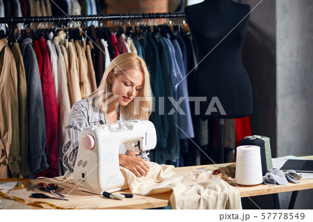 awesome woman sitting at the table and sews on sewing machine. 57778549