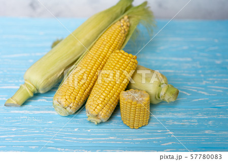 Corn cob with green leaves lies on table blue Corn cob with green leaves lies on table blue 57780083