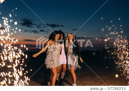 Group of happy girlfriends dancing between fireworks at night 57780253