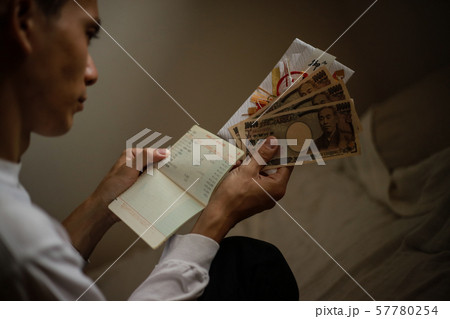 通帳を見ながらご祝儀を悩む男性 通帳を見ながらご祝儀を悩む男性 57780254