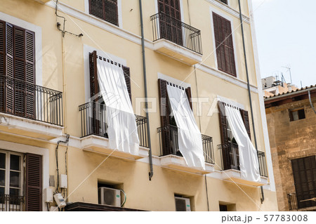 マヨルカ島の街並み　茶色の遮光扉と日よけのシーツの付いた窓のある薄クリーム色の建物 57783008