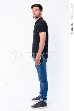 Full body shot profile view of young bearded Persian man looking at camera 57799902